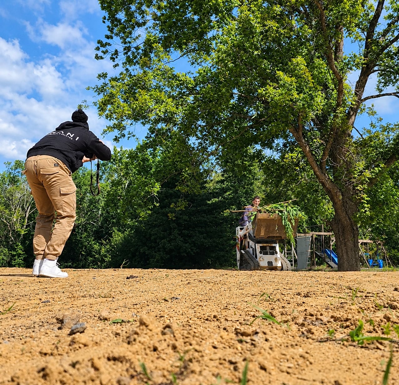 Yvad Brown crouched on a graded lot, photographing a skid steer operator clearing brush